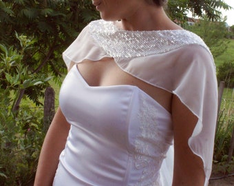 May include: A bride wearing a white wedding dress with a sheer lace overlay and a beaded neckline. She is wearing a sparkling hairpiece and has her hair pulled back.