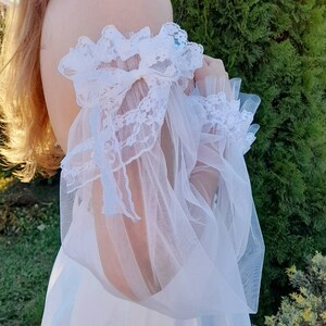 K&ouml;nnte beinhalten: Wei&szlig;es, schulterfreies Kleid mit durchsichtigen Spitzen&auml;rmeln und einem Schleifendetail.