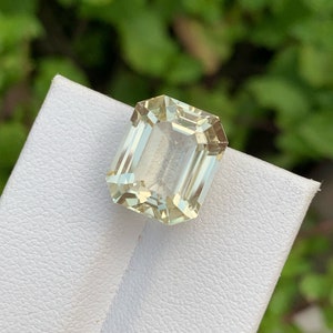 Pode incluir: Uma gema verde clara cortada em esmeralda em um suporte de exibi&ccedil;&atilde;o branco.
