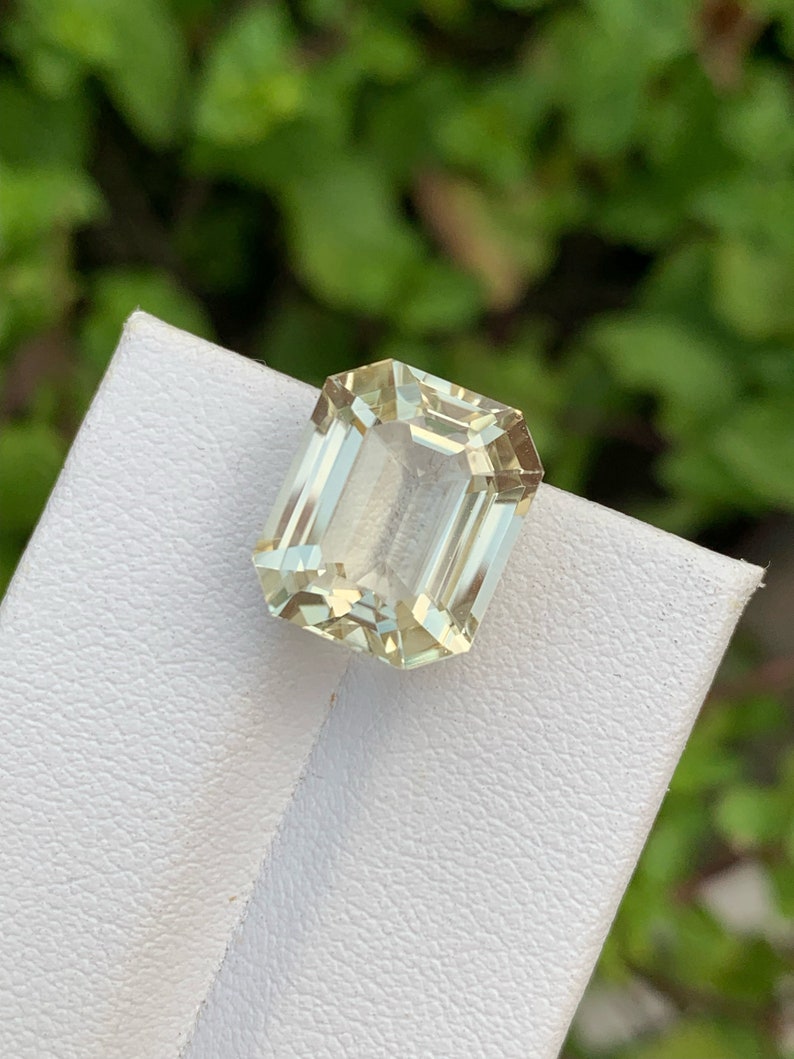 Pode incluir: Uma gema verde clara cortada em esmeralda em um suporte de exibi&ccedil;&atilde;o branco.