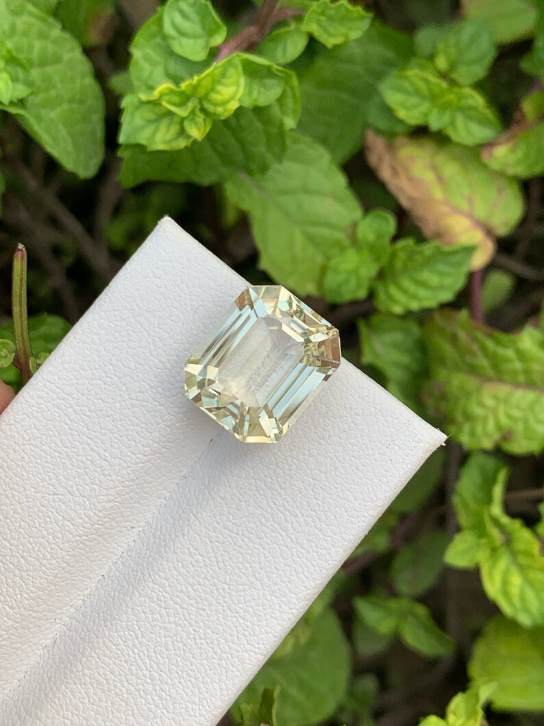 Pode incluir: Uma gema verde clara cortada em esmeralda em um fundo branco.