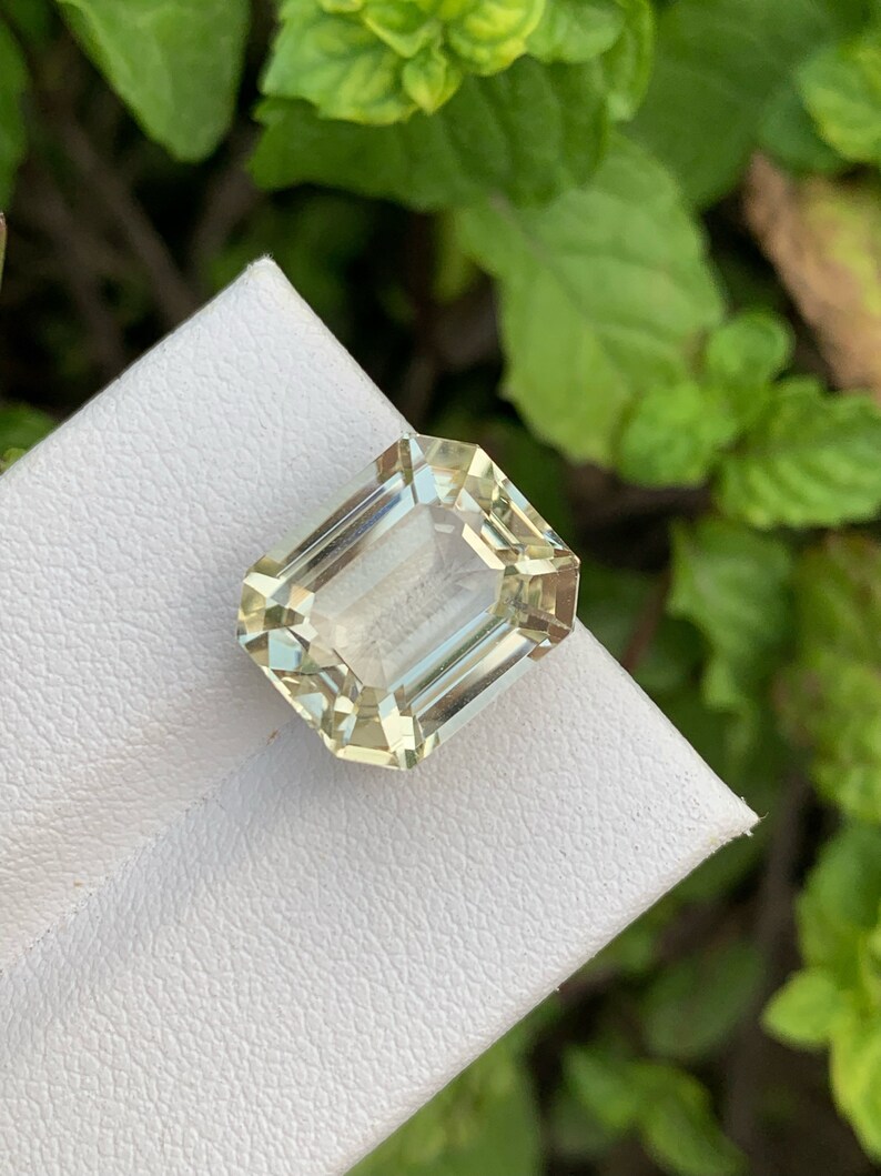 Pode incluir: Uma gema verde clara cortada em esmeralda em um fundo branco.