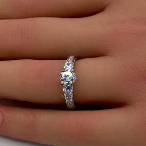 Puede incluir: Un anillo de plata con una piedra redonda grande transparente y piedras transparentes más pequeñas en la banda.