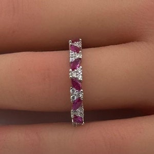 May include: A silver band ring with alternating pink marquise-shaped gemstones and round white gemstones.