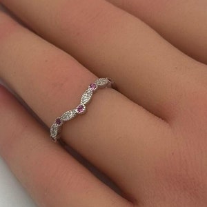 May include: A delicate silver band ring with a wavy design and small pink gemstones set in the band.