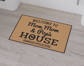May include: A rectangular doormat with the text "WELCOME TO Mom Mom & Pop's HOUSE GRANDKIDS SPOILED HERE" in black on a tan background. The mat is placed in a doorway on a light wood floor.