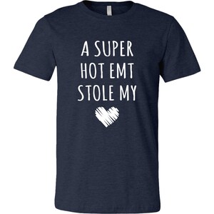 May include: A navy blue t-shirt with white text that reads "A super hot EMT stole my" with a white heart graphic below the text.