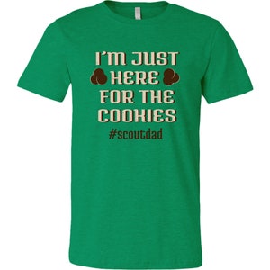 May include: Green t-shirt with the text "I'm just here for the cookies #scoutdad" in brown and beige text.