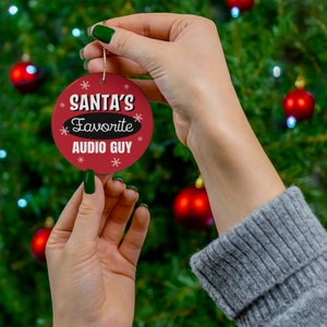 May include: Red and white Christmas ornament with the text "Santa's Favorite Audio Guy" surrounded by snowflakes.
