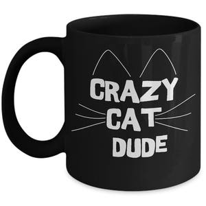 May include: Black coffee mug with white text that reads "Crazy Cat Dude" and a stylized cat face with whiskers.