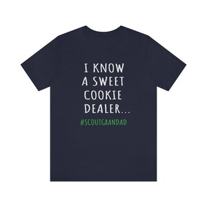 Op de afbeelding: Donkerblauw T-shirt met witte tekst die luidt "Ik ken een zoete koekjesdealer... #ScoutGrandad".