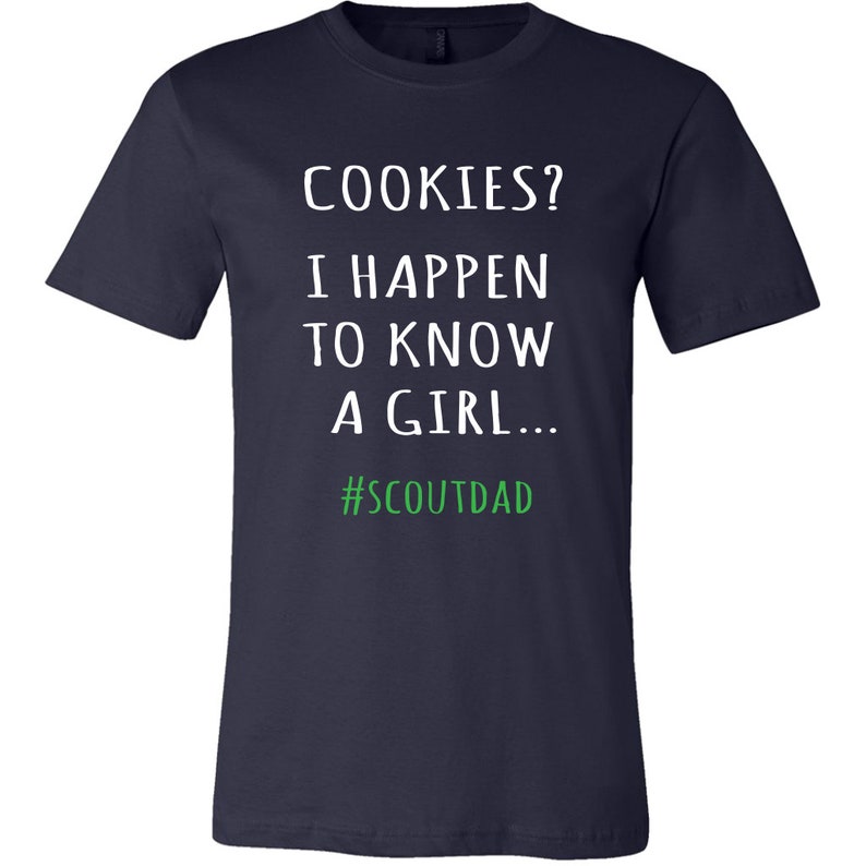 May include: Navy blue t-shirt featuring the text "COOKIES? I HAPPEN TO KNOW A GIRL..." in white, with the hashtag "#SCOUTDAD" in green. A casual style t-shirt.