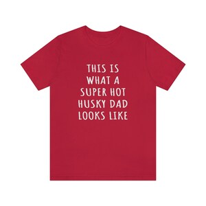 May include: Red t-shirt with white text that reads "This is what a super hot husky dad looks like."