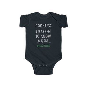 May include: A dark blue baby onesie with white text that reads "COOKIES? I HAPPEN TO KNOW A GIRL... #SCOUTSISTER".