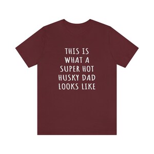 May include: A maroon t-shirt with white text that reads "This is what a super hot husky dad looks like."