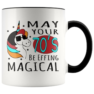 May include: White ceramic coffee mug with a black rim and handle. The mug features a colorful illustration of a unicorn wearing sunglasses and the text "May your 70's be effing magical."