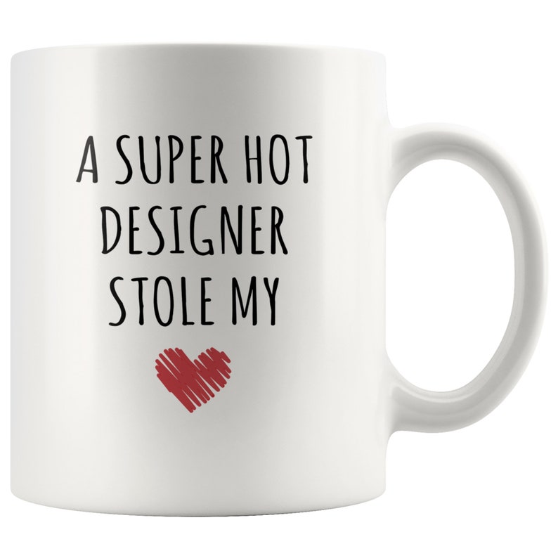May include: White ceramic mug with the text "A SUPER HOT DESIGNER STOLE MY" in black, with a red heart graphic. The mug has a curved handle and is designed for hot beverages.