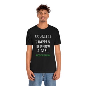 May include: A black t-shirt with white text that reads "COOKIES? I HAPPEN TO KNOW A GIRL... #SCOUTNEIGHBOR".