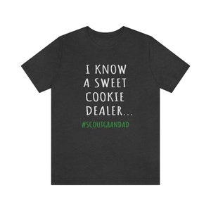 Op de afbeelding: Donkergrijs T-shirt met witte tekst die "Ik ken een zoete koekjesdealer... #ScoutGrandad" in groen zegt.