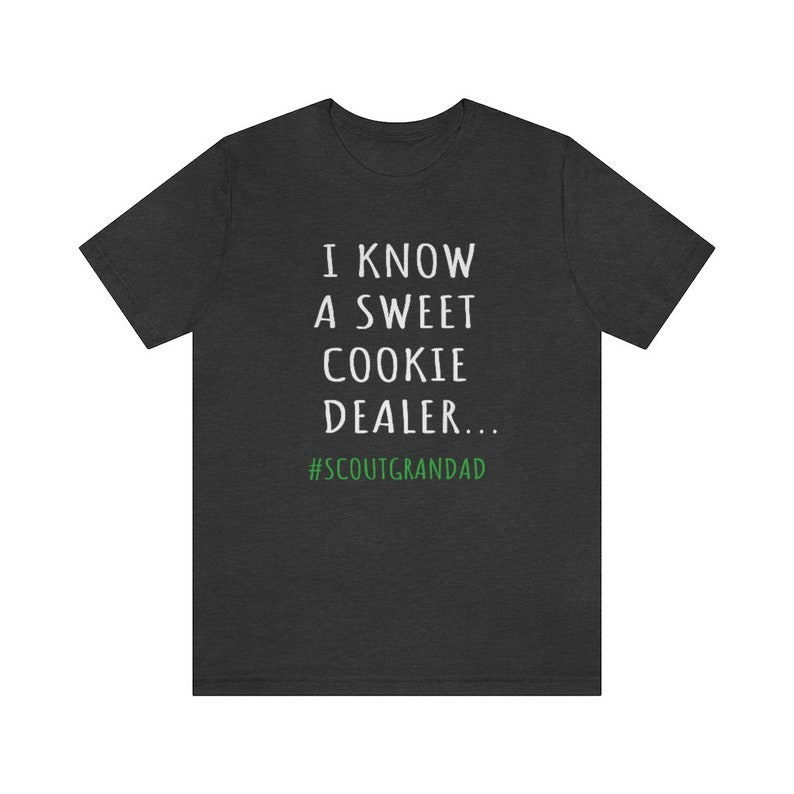 Op de afbeelding: Donkergrijs T-shirt met witte tekst die "Ik ken een zoete koekjesdealer... #ScoutGrandad" in groen zegt.