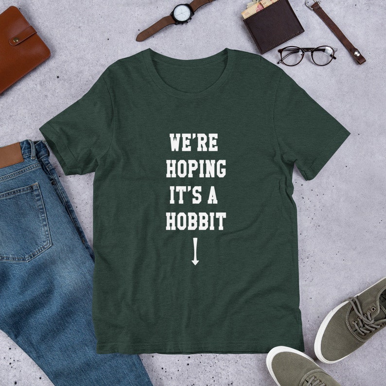 Może przedstawiać: Zielony t-shirt z białym napisem "We're Hoping It's A Hobbit" ze strzałką skierowaną w d&oacute;ł.
