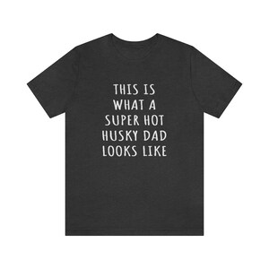 May include: Dark heather grey t-shirt with white text that reads "This is what a super hot husky dad looks like."