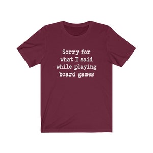 May include: A maroon t-shirt with white text that reads "Sorry for what I said while playing board games".