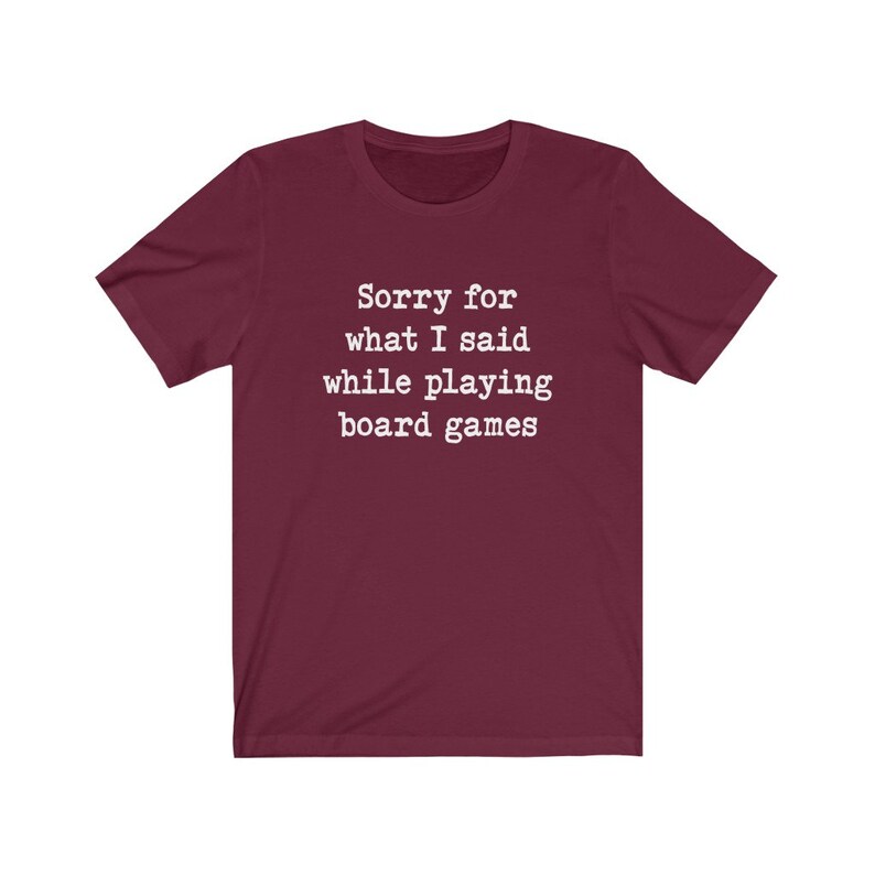 May include: A maroon t-shirt with white text that reads "Sorry for what I said while playing board games".