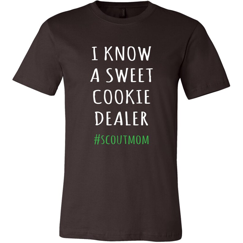 May include: A dark brown t-shirt with white text that reads "I know a sweet cookie dealer #scoutmom" in green.