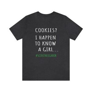 May include: Dark heather grey t-shirt with white text that reads "COOKIES? I HAPPEN TO KNOW A GIRL... #SCOUTNEIGHBOR".