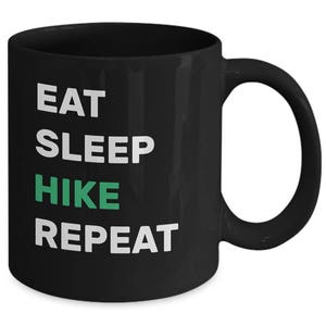May include: Black coffee mug with white text that reads "Eat Sleep Hike Repeat". The word "Hike" is in green.