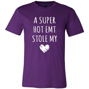 May include: Purple t-shirt with white text that reads "A super hot EMT stole my" with a white heart graphic below the text.