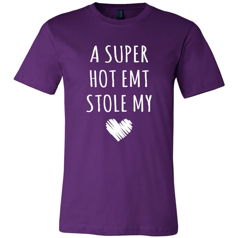 May include: Purple t-shirt with white text that reads "A super hot EMT stole my" with a white heart graphic below the text.