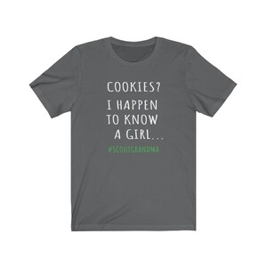 Puede incluir: Camiseta gris oscuro con texto blanco que dice "COOKIES? I HAPPEN TO KNOW A GIRL... #SCOUTGRANDMA".