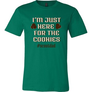 May include: Green t-shirt with the text "I'm just here for the cookies #scoutdad" in brown text. Two brown cookie images are above the word "here".