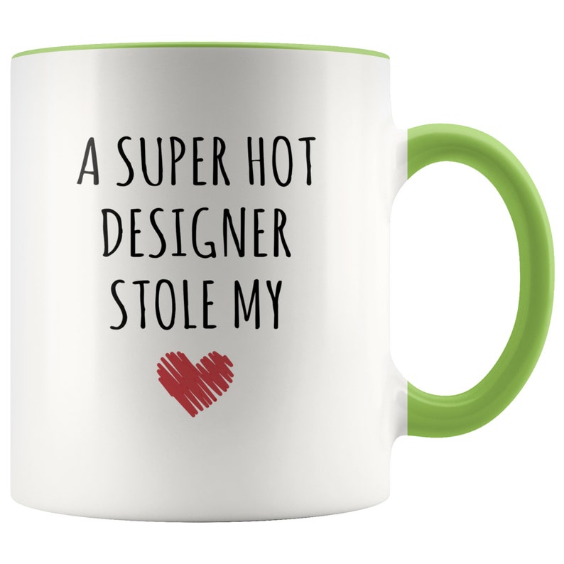 May include: White ceramic mug with a green handle and interior rim. The mug features the text "A SUPER HOT DESIGNER STOLE MY" in black, with a red heart graphic below the text. A fun gift for a designer.