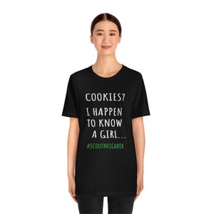 May include: Black t-shirt with white text that reads "COOKIES? I HAPPEN TO KNOW A GIRL... #SCOUTNEIGHBOR"