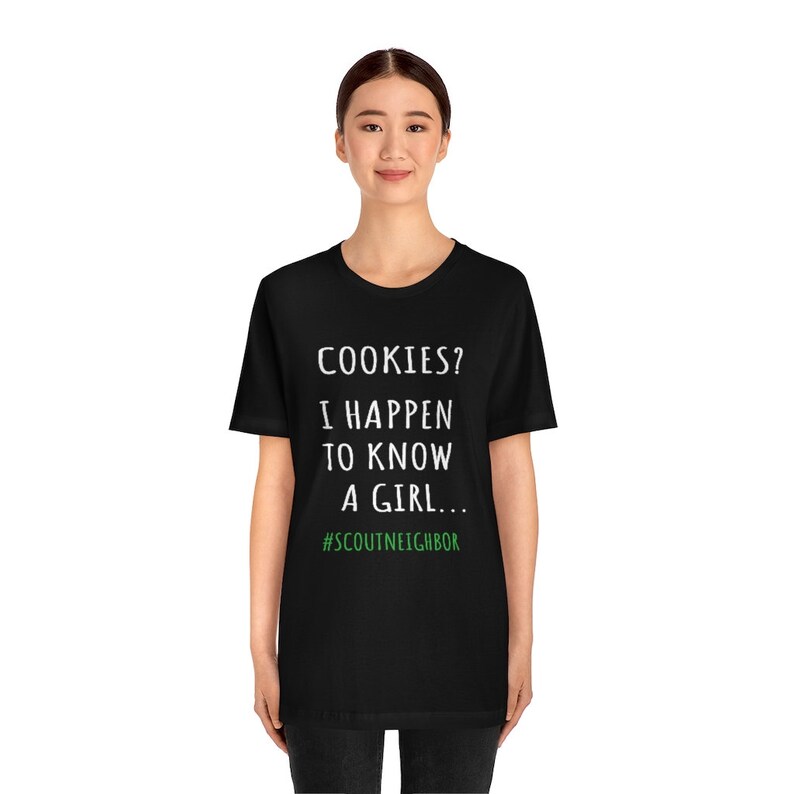 May include: Black t-shirt with white text that reads "COOKIES? I HAPPEN TO KNOW A GIRL... #SCOUTNEIGHBOR"
