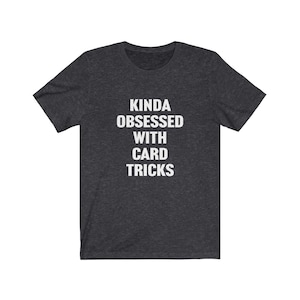 May include: A dark heather grey t-shirt with the text "Kinda obsessed with card tricks" printed in white.