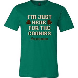 May include: Green t-shirt with the text "I'm Just Here For The Cookies" and the hashtag "#scoutmom".