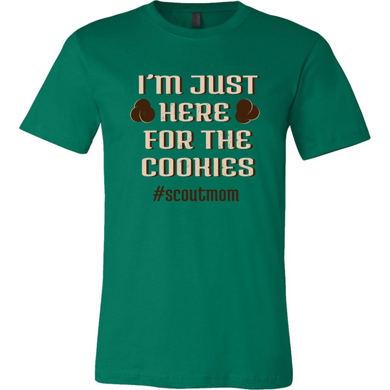 May include: Green t-shirt with the text "I'm Just Here For The Cookies" and the hashtag "#scoutmom".