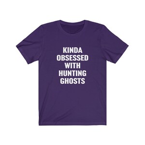 May include: Purple short-sleeved t-shirt with white text that reads "Kinda obsessed with hunting ghosts".