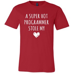 Pu&ograve; includere: Maglietta rossa con testo bianco che recita "A super hot programmer stole my" con un cuore bianco disegnato sotto.