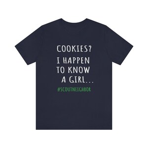 May include: Navy blue t-shirt with white text that reads "COOKIES? I HAPPEN TO KNOW A GIRL... #SCOUTNEIGHBOR".