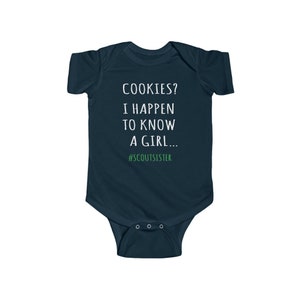 May include: A dark blue baby onesie with white text that reads "COOKIES? I HAPPEN TO KNOW A GIRL... #SCOUTSISTER".