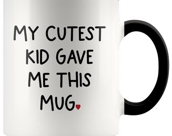 May include: White ceramic mug with a black rim and handle. The mug has black text that reads "My Cutest Kid Gave Me This Mug" with a small red heart.