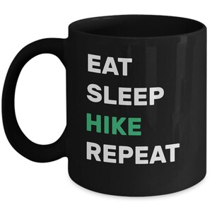 May include: Black coffee mug with white text that reads "Eat Sleep Hike Repeat" with the word "Hike" in green.