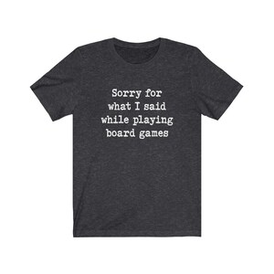 May include: Dark heather grey t-shirt with white text that reads "Sorry for what I said while playing board games".