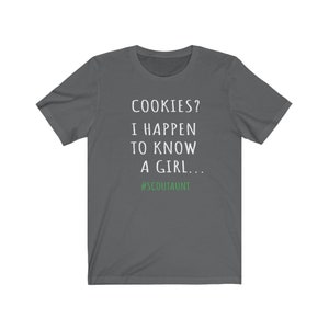 May include: Dark gray t-shirt with white text that reads "COOKIES? I HAPPEN TO KNOW A GIRL... #SCOUTAUNT"
