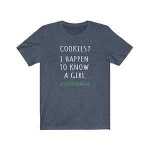 Puede incluir: Una camiseta azul oscuro con texto blanco que dice "COOKIES? I HAPPEN TO KNOW A GIRL... #SCOUTGRANDMA". El texto "#SCOUTGRANDMA" est&aacute; en verde.